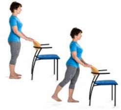 Woman standing behind a chair and holding onto it lightly with both hands. Underneath the same woman is holding onto the chair whilst bringing one leg back whilst keeping the leg sraight.