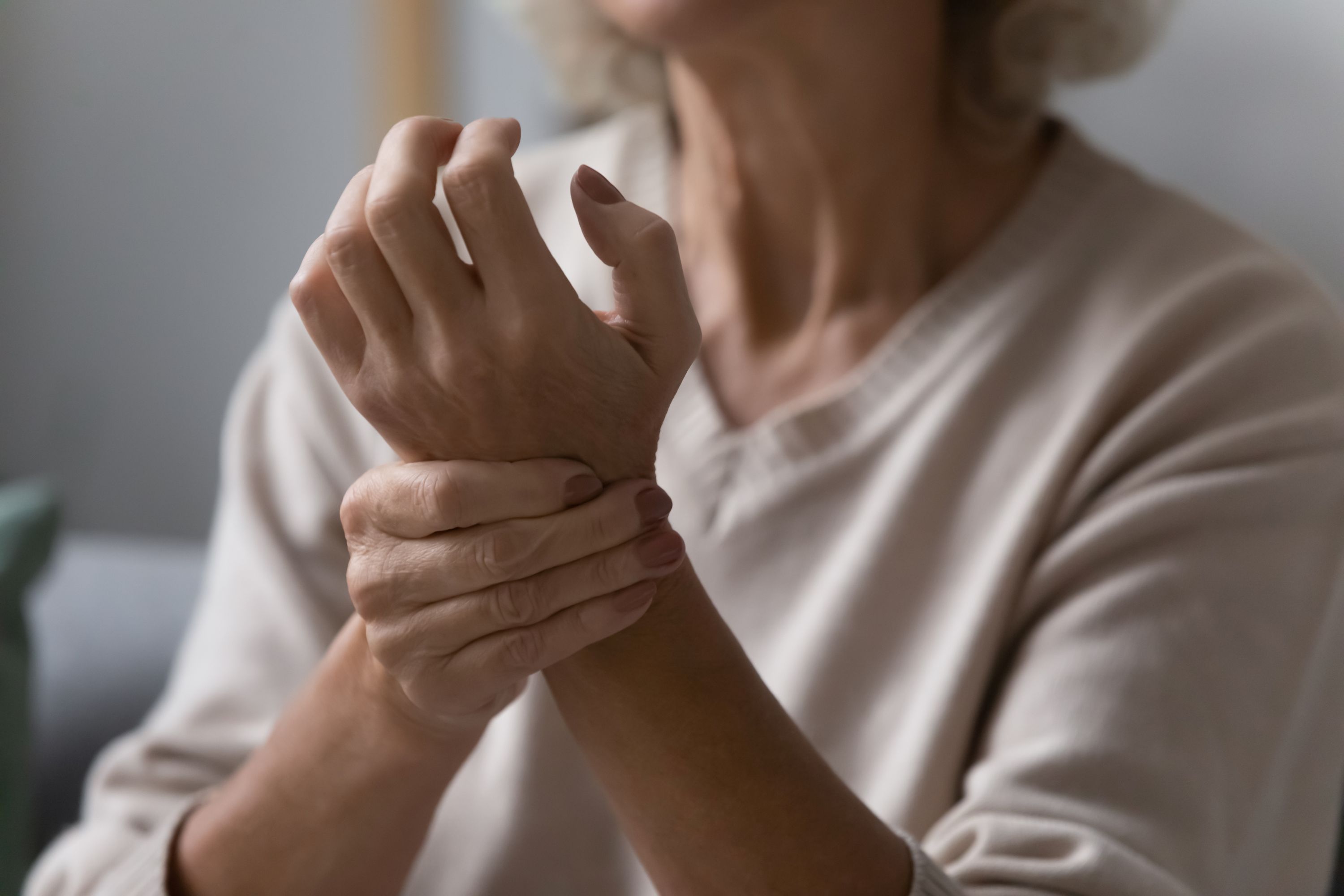 Elderly white woman wearing a cream jumper clutches her wrist due to nerve pain