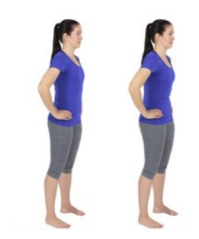 a young woman standing on a exercise mat in a purple t-shirt. She stands with legs hip distance apart and pulls the angle of her lower back to create a posterior pelvic tilt while standing. 