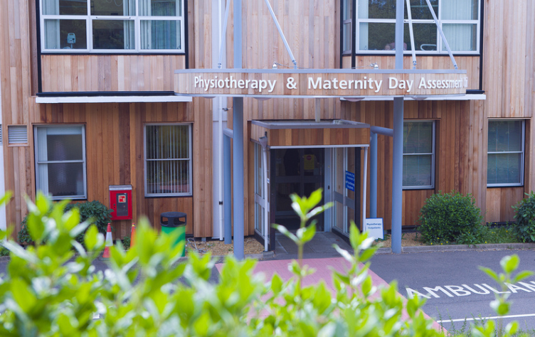 Hinchingbrooke Physiotherapy site entrance of a wood panelled building with a sign saying physiotherapy and maternity day assessment.